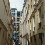 Dualité des couleurs de la ville. L’ilot de Beaubourg a été cureté pour laisser la place au Centre Georges Pompidou. Comme les cathédrales gothiques, ce palais est fier de montrer ses audaces techniques. Il est reconnaissable à ses tubulures colorées signalant la circulation des fluides. L’angle de vue retient l’enfilade des rues étroites, peu éclairées et mal alignées du IVe Arrondissement. Elles furent épargnées par les grands travaux haussmanniens et contribuent au charme de Paris (cliché J.-P. H).