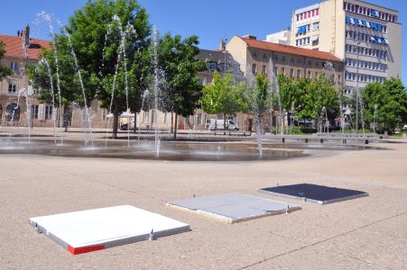 Au premier plan : mires thermiques utilisées pour le calibrage de la caméra infra-rouge embarquée sur le drone. Au second plan : fontaines urbaines à jets d’eau, arbres et bosquet.